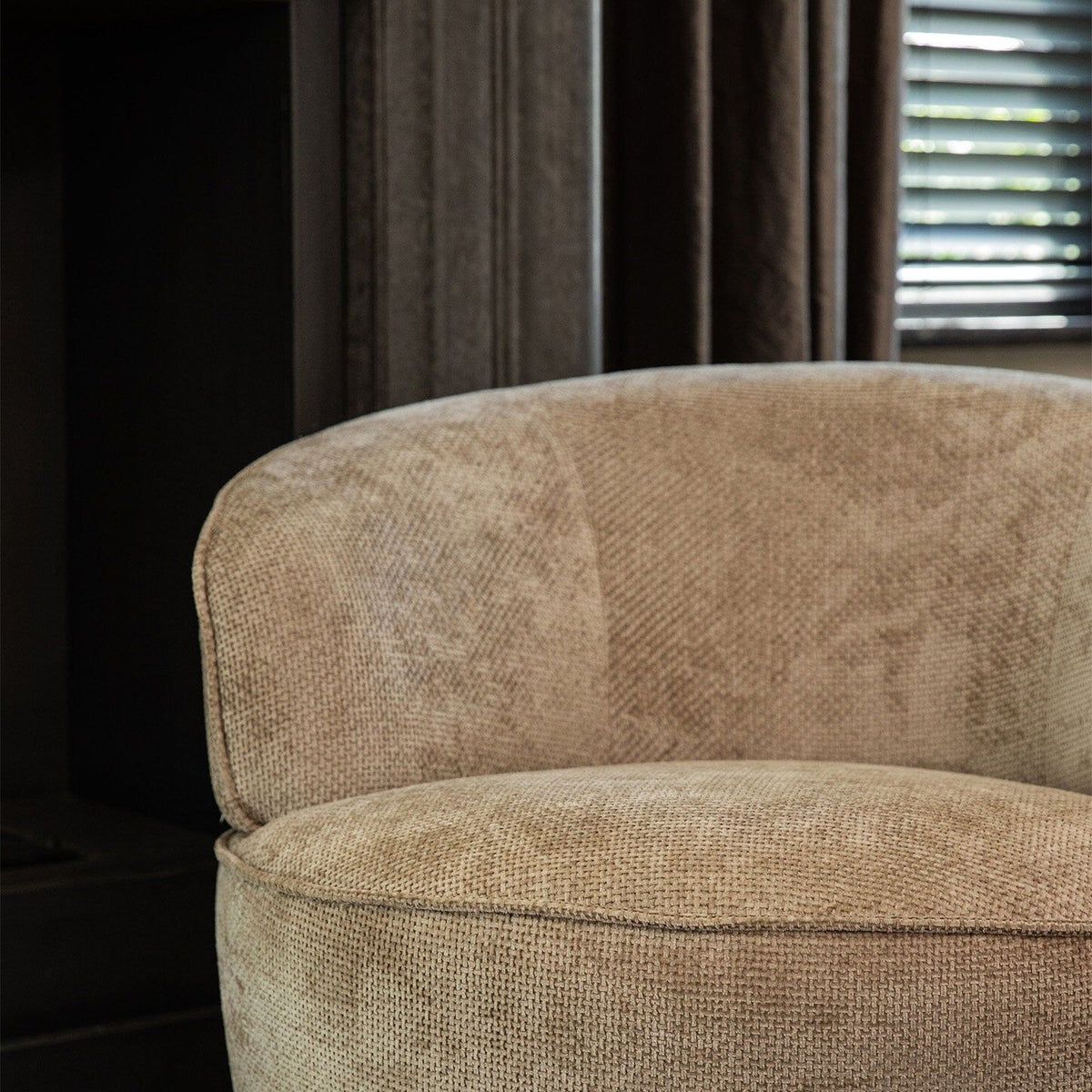 Beige Filou draaifauteuil van PTMD in een interieur met donkere gordijnen