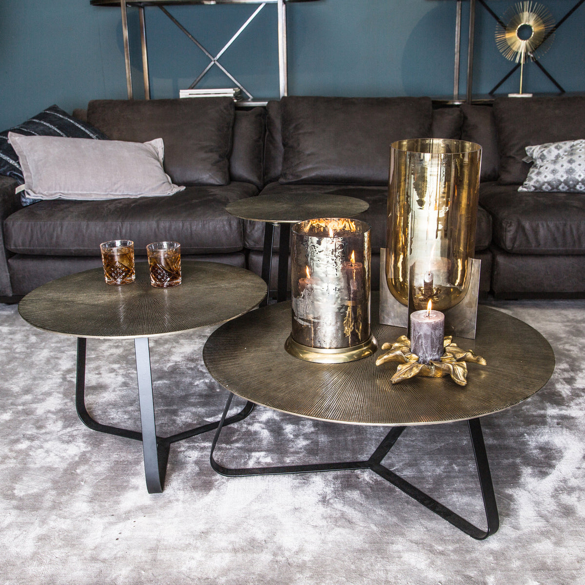 Drie Kae tafels van PTMD met goud aluminium blad in een woonkamer met donkere bank en gouden vazen
