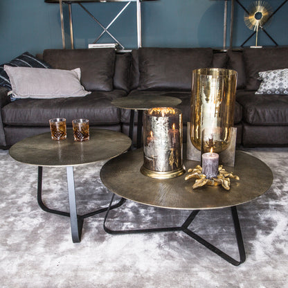Drie Kae tafels van PTMD met goud aluminium blad in een woonkamer met donkere bank en gouden vazen