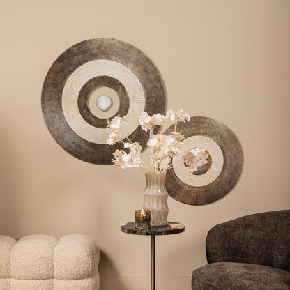 Wandpaneel Jacci Goud Rond Small van PTMD, twee panelen aan een beige muur boven een bijzettafel met bloesem